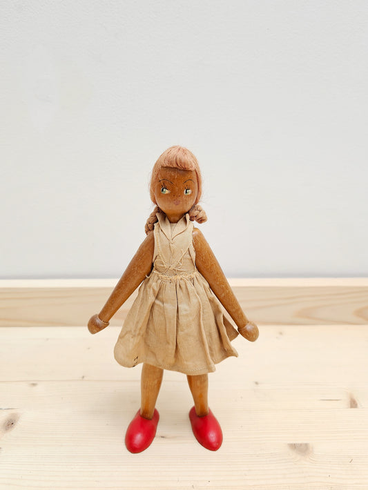 Vintage Polish wooden peg doll, wearing taupe handmade dress, beautifully painted face, against a white wall.