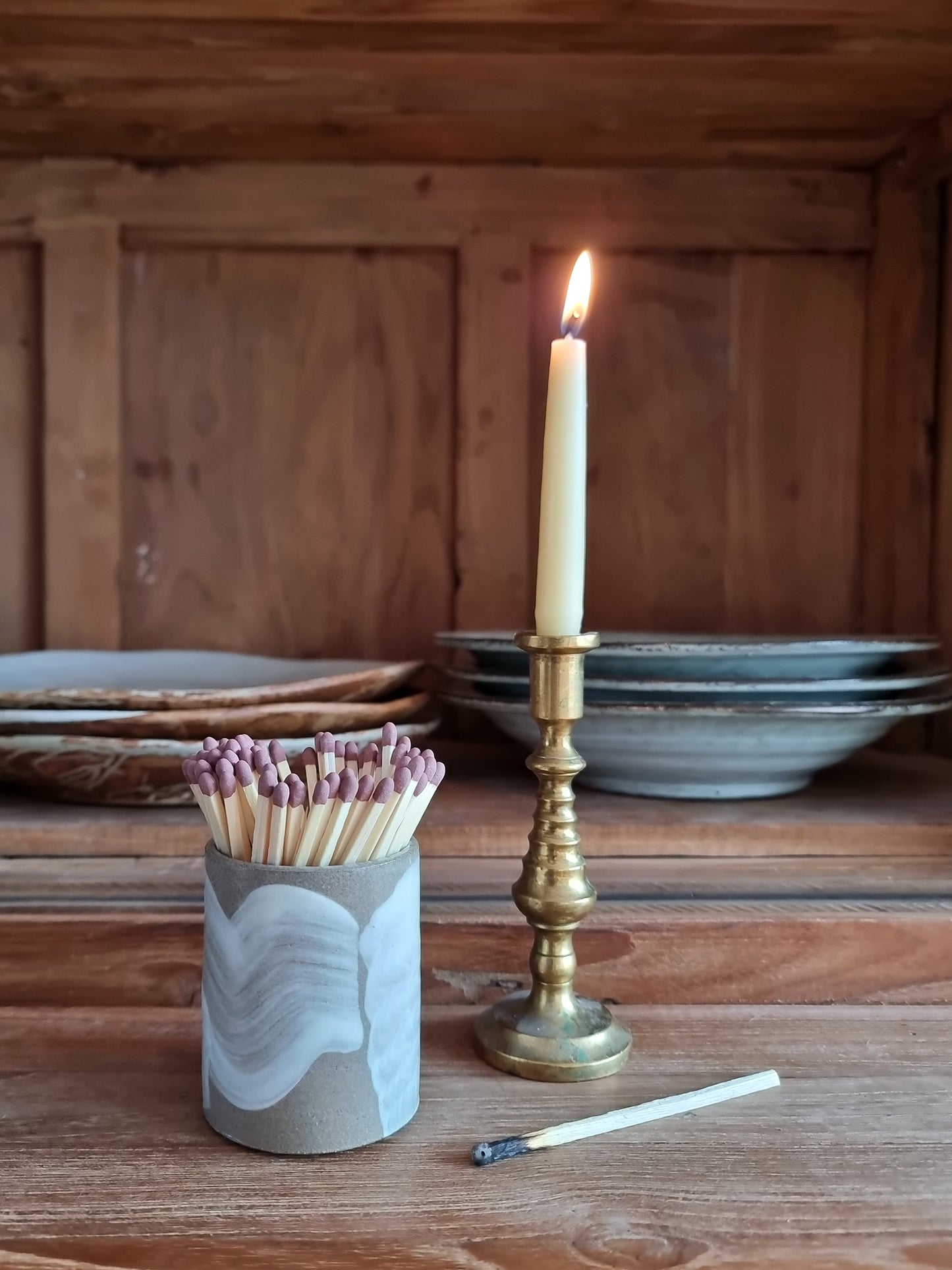 Handmade brushstroke match pot by Bel Holland filled with extra long matches, styled beside a lit taper candle in a brass candlestick