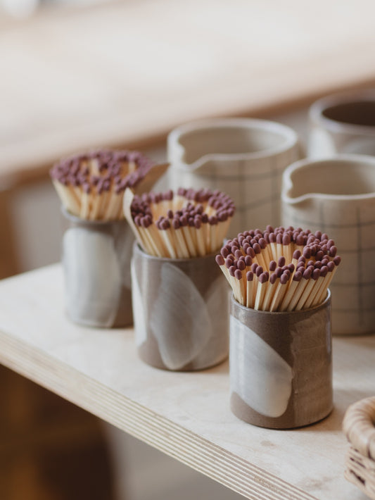 Three Bel Holland brushstroke match pots filled with extra long matches, displayed on a shop shelf alongside handmade ceramics