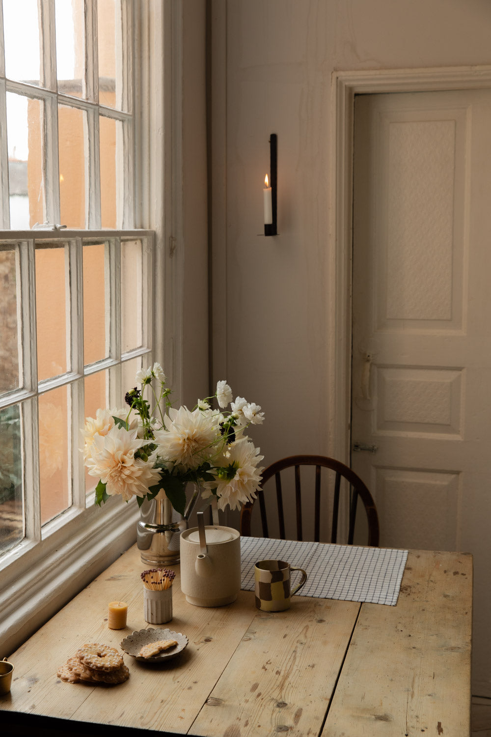 Kitchen corner with a black wall candle holder, dahlias and a table set for tea