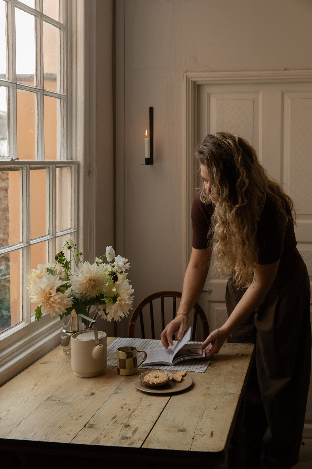 Woman reading at a table lit by a black wall candle holder