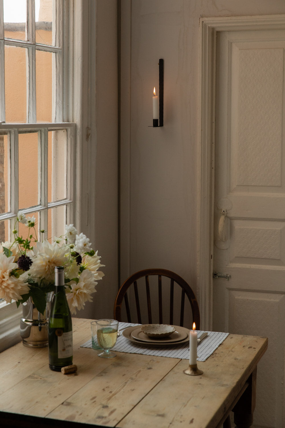 Lit candle in a black wall candle holder above a table set with wine and dahlias
