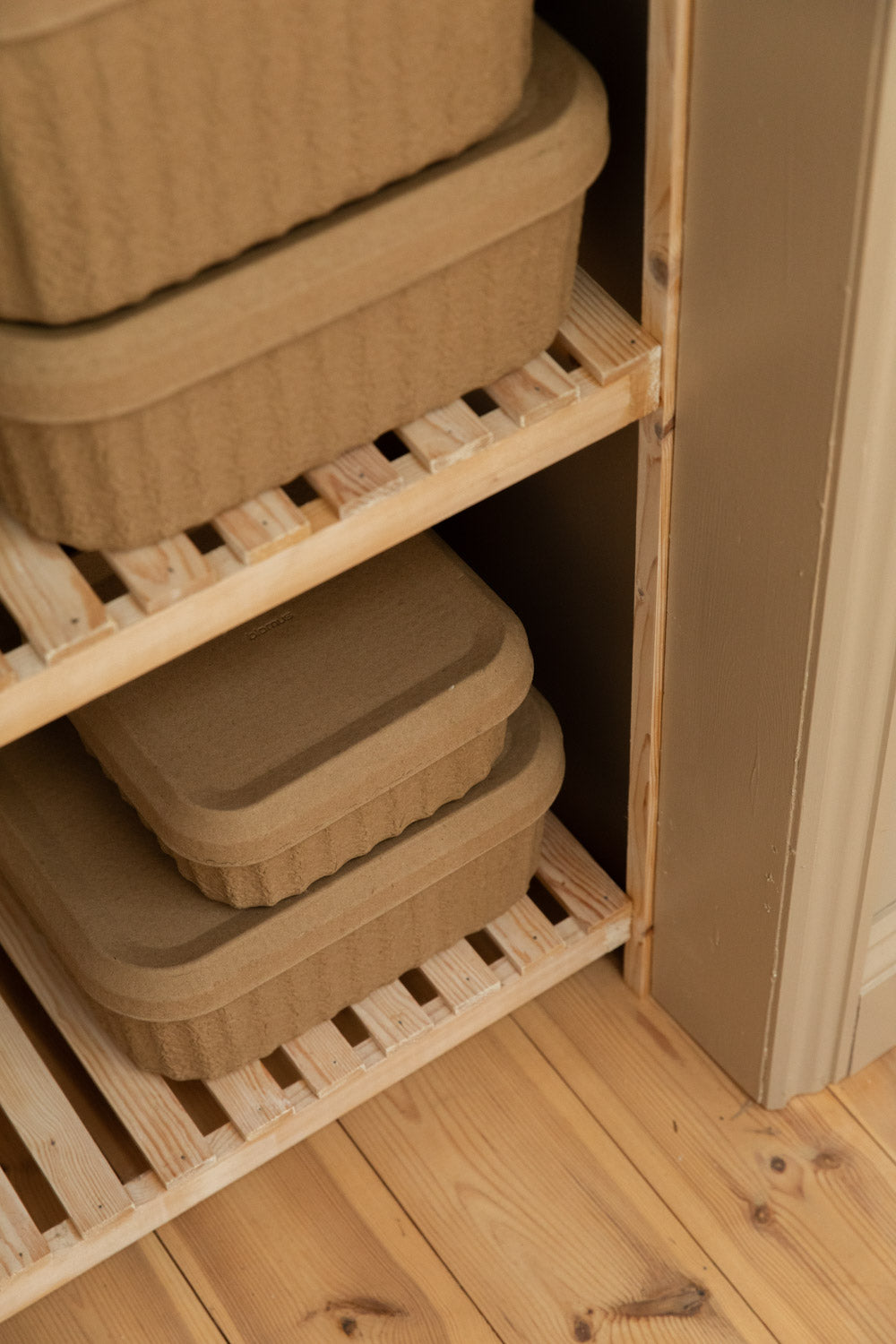 Close-up of Blomus Redo paper pulp storage boxes in two sizes stacked on slatted pine wardrobe shelves.
