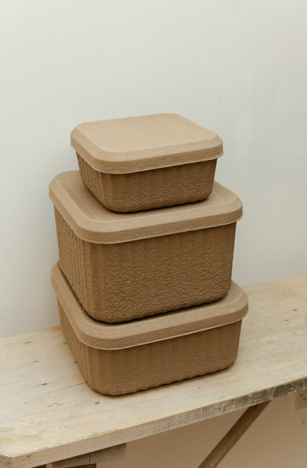 Angled close-up of three Blomus Redo paper pulp storage boxes stacked by size on a rustic pale wood table showing textured surface detail.