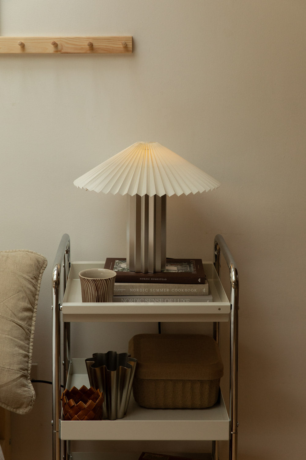 Blomus Taite lamp in lily white on chrome trolley styled with Nordic books, striped ceramic cup and steel vase on lower shelf.