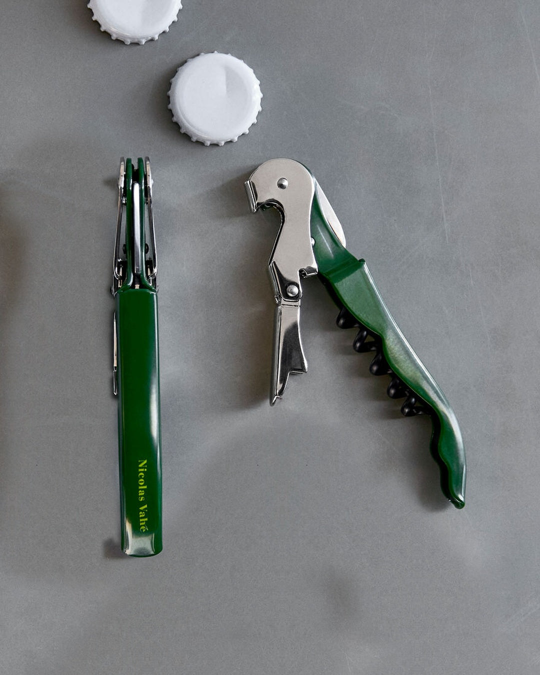 Green Nicolas Vahé bottle opener, open and closed, on grey concrete
