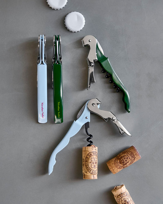 Green and light blue Nicolas Vahé bottle openers with corks and bottle caps on grey concrete