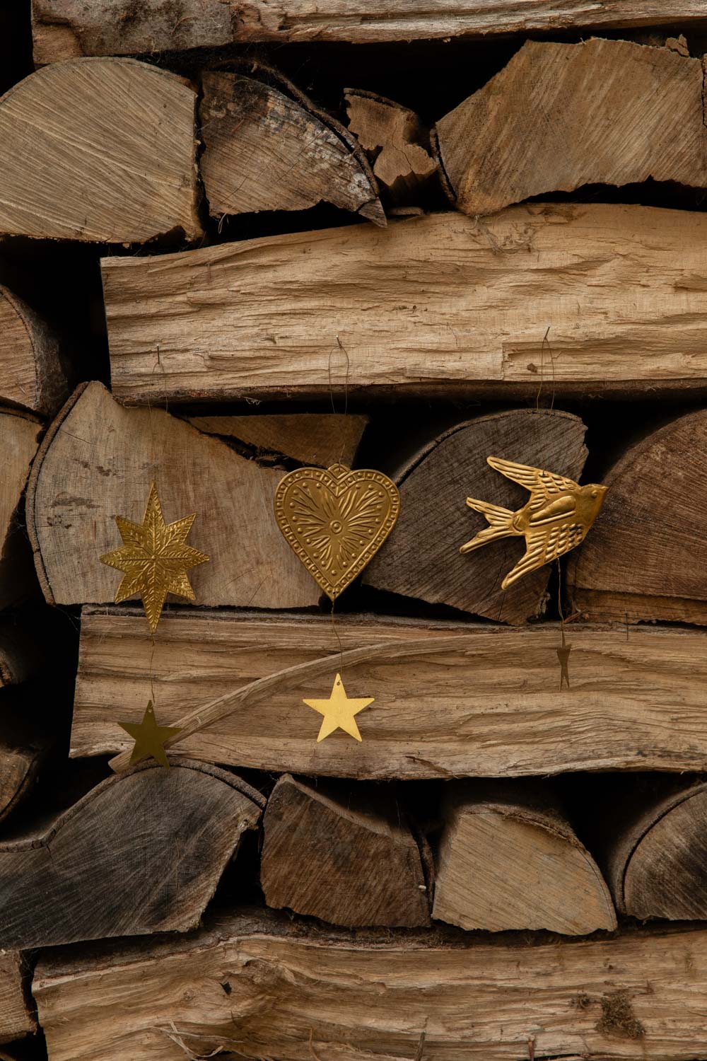 Embossed brass star, heart and swallow decorations hung on stacked logs