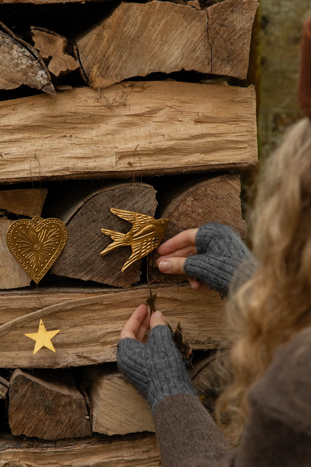 Hands placing embossed brass heart and bird decorations on a log pile