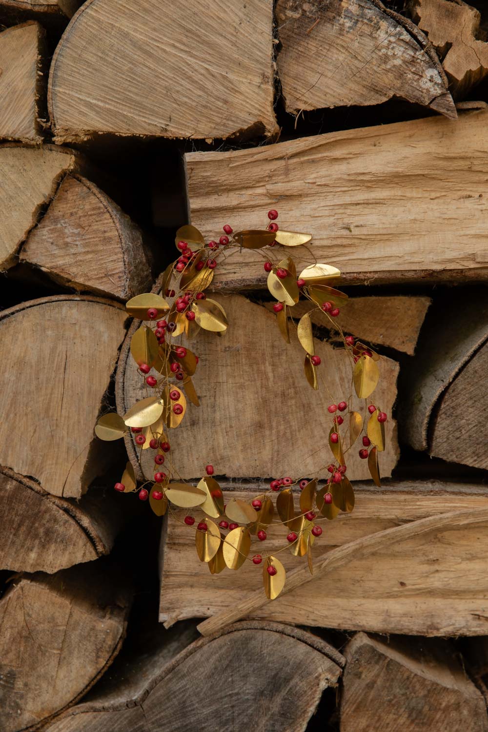 Brass Red Berry Garland of golden leaves and red beads looped into a wreath on a log pile