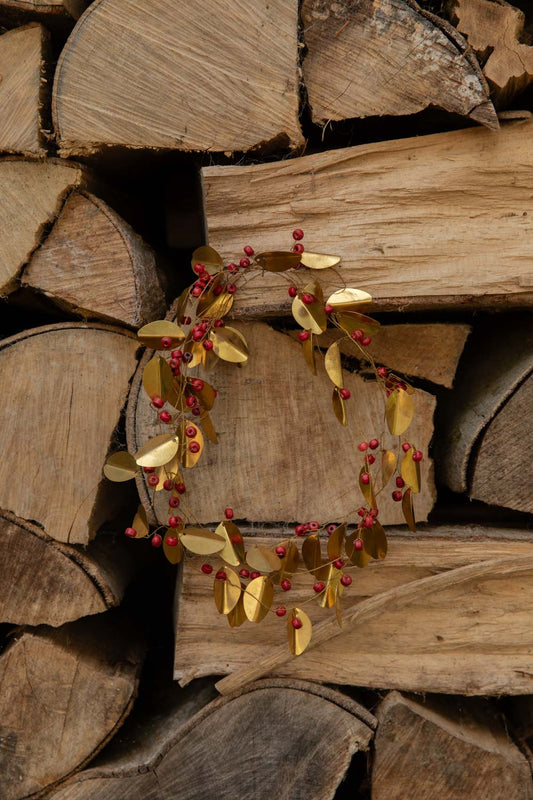 Brass Red Berry Garland of golden leaves and red beads looped into a wreath on a log pile
