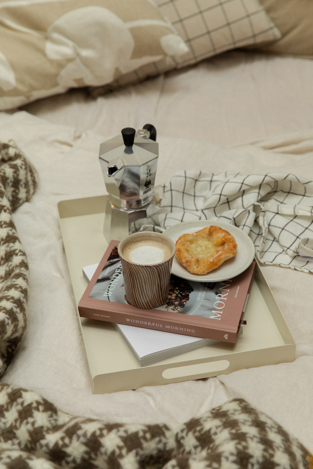 Bricka off-white tray styled with Diva stripe mug, Bialetti Moka Express and pastry on a bed with houndstooth wool blanket and grid linen.