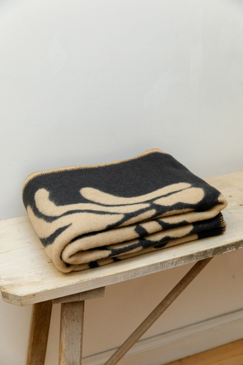 Brita Sweden Pine lambswool blanket in dark blue and sand folded neatly on a rustic pale wood table.
