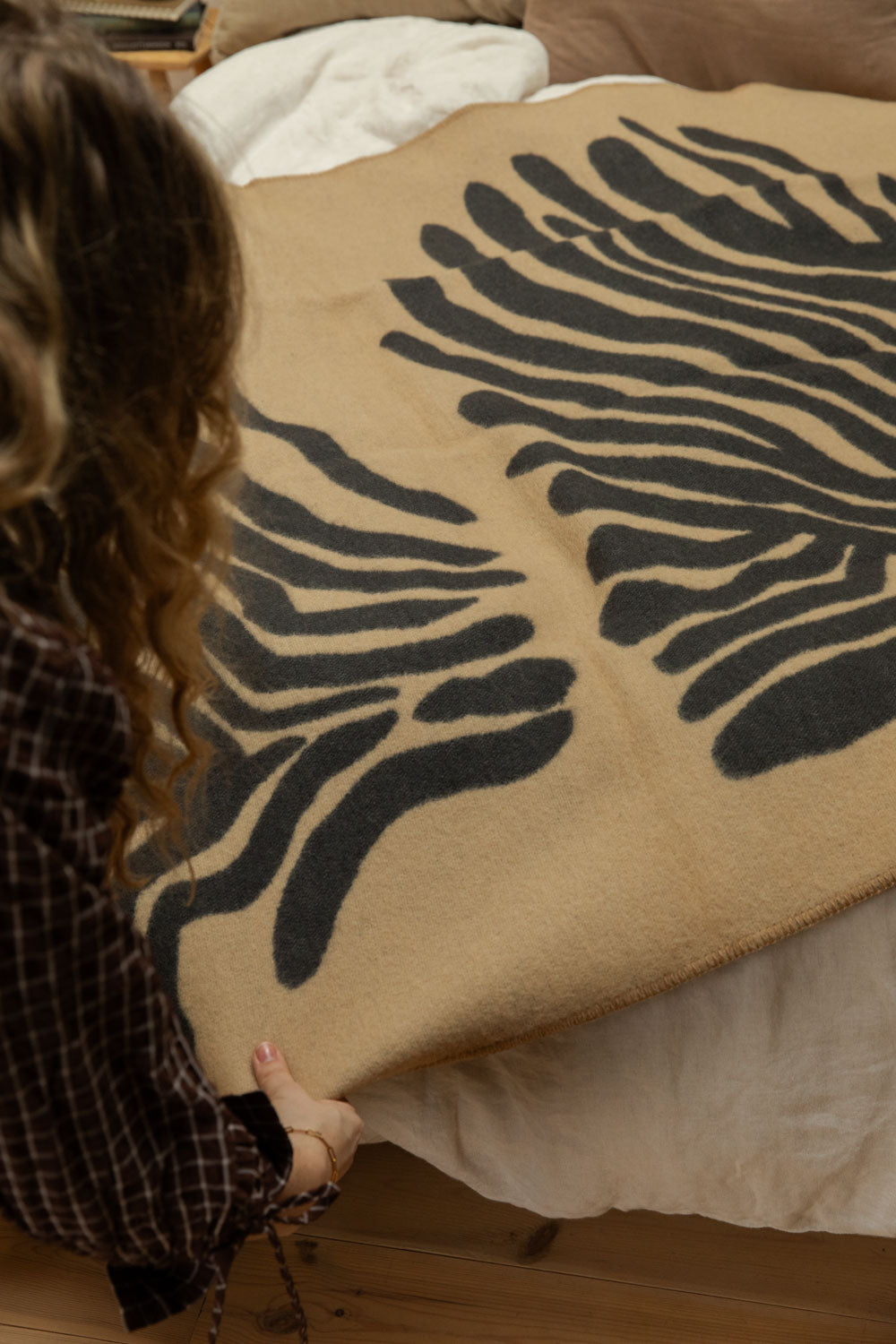 Overhead view of hands holding Brita Sweden Pine lambswool blanket in sand and dark blue showing abstract fern print detail.
