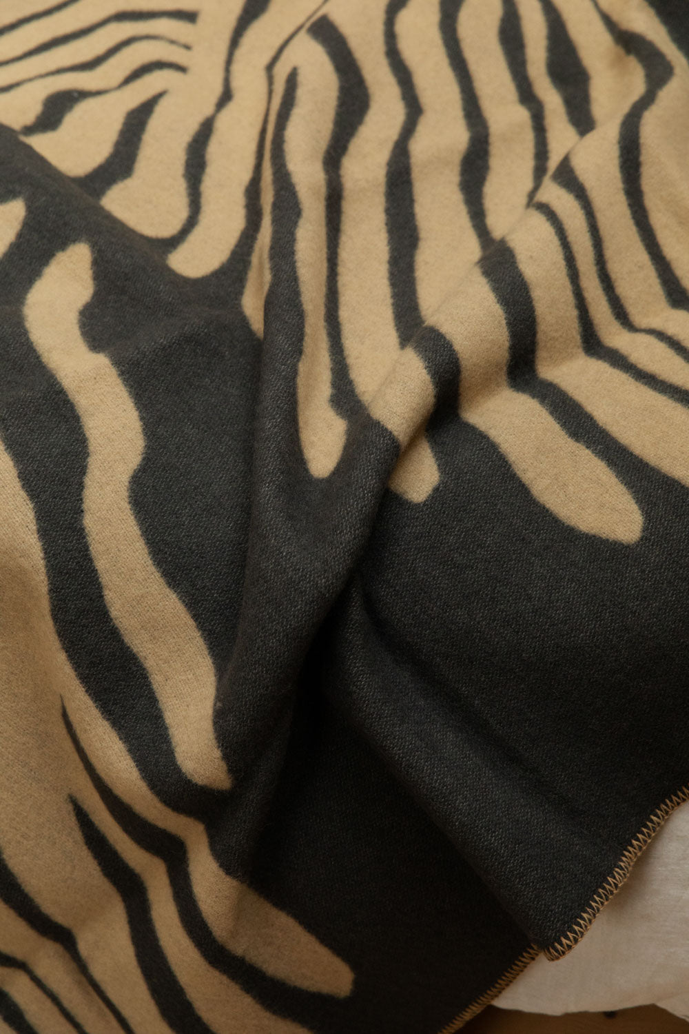 Close-up of Brita Sweden Pine lambswool blanket in sand and dark blue showing abstract fern print and soft brushed texture detail while draped.