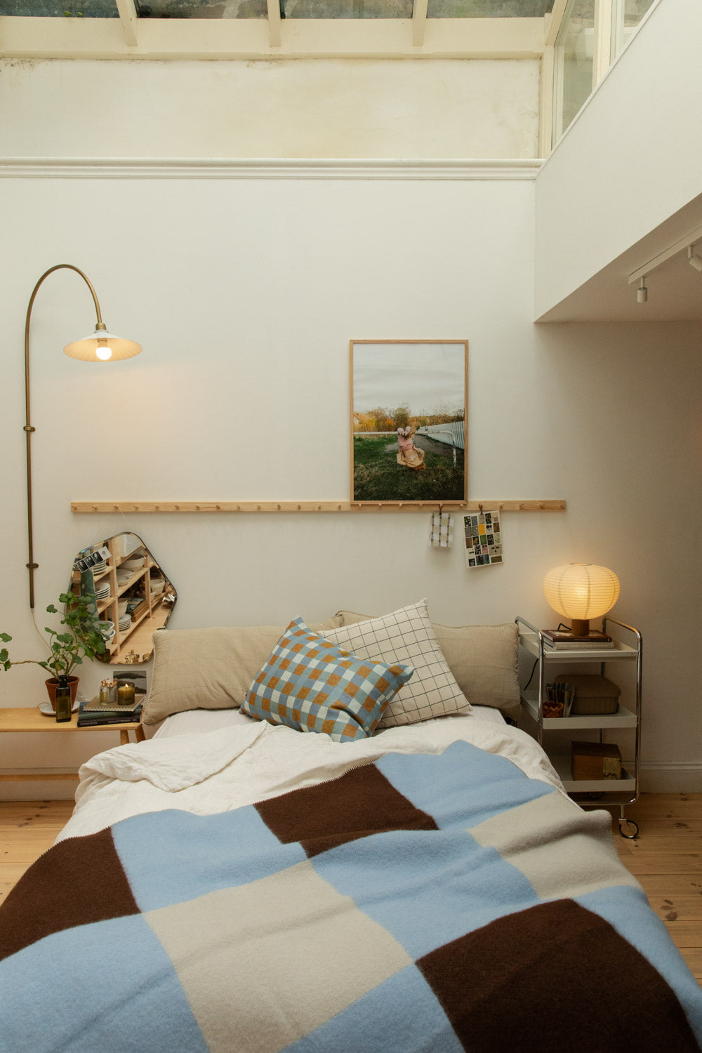 Full bedroom view with Brita Sweden Pop lambswool blanket in blue and brown on a bed styled with Fine Little Day Rutan linen cushion, pine shaker peg rail, arc floor lamp and paper lantern table lamp.