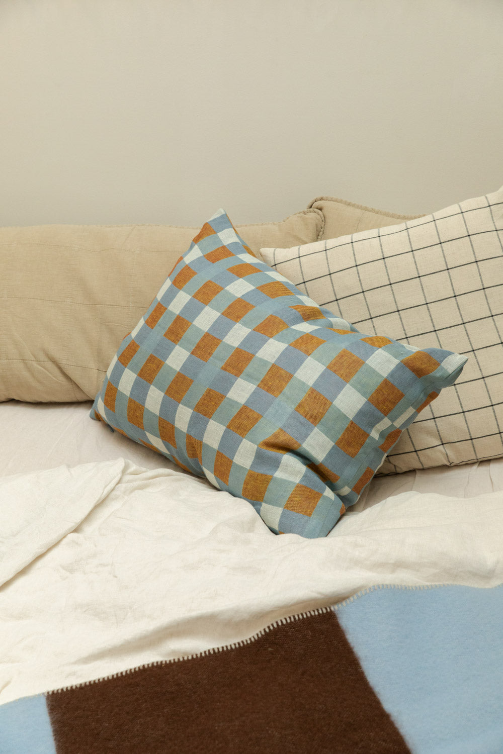 Brita Sweden Pop lambswool blanket in blue and brown draped over a bed styled with Fine Little Day Rutan linen cushion cover in blue and mustard check and House Doctor Join grid check cushion.