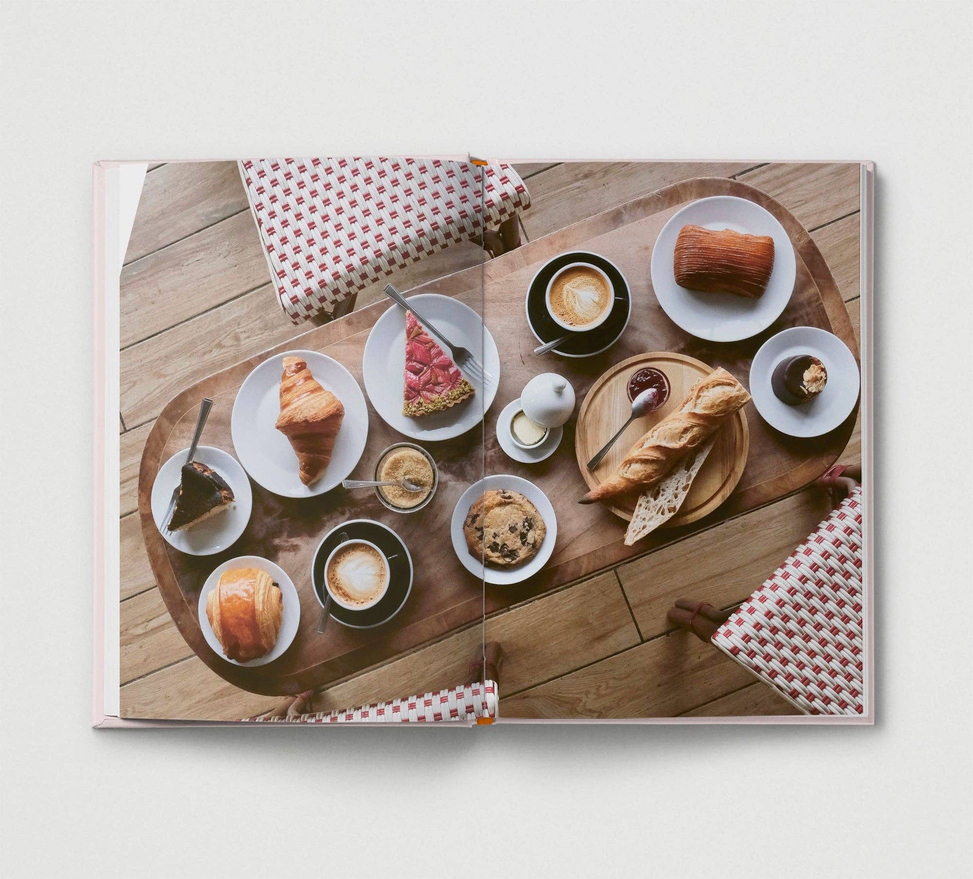Open book showing a wooden table with various pastries and coffee cups on a white background.
