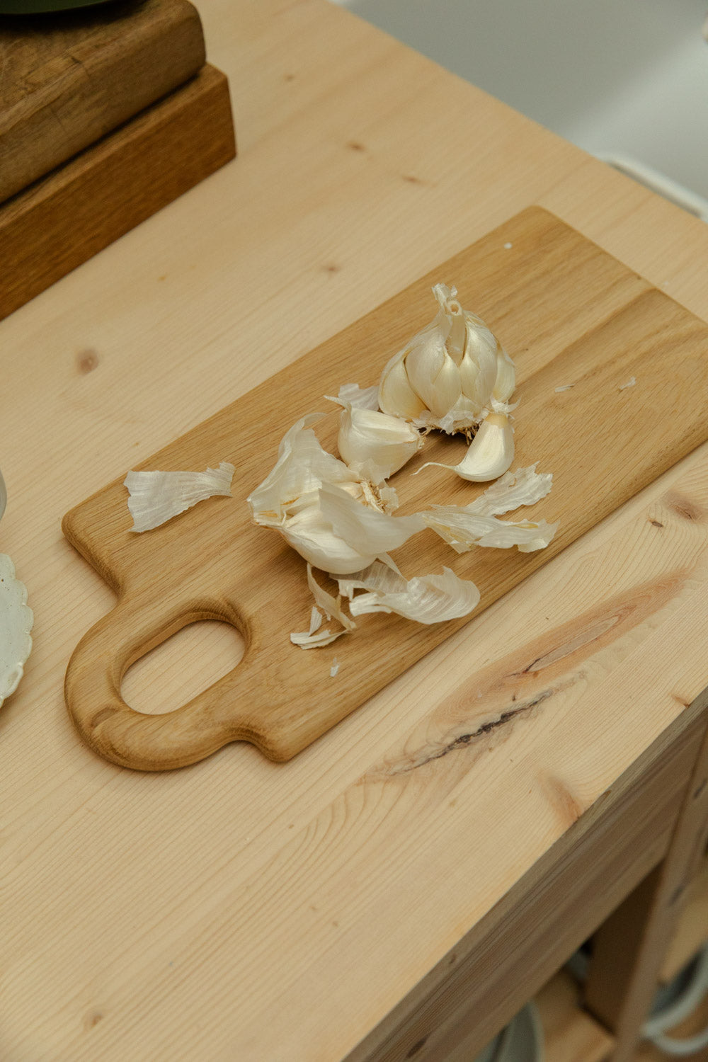 Broste Copenhagen Olina oak chopping board with torn garlic pieces scattered on top.