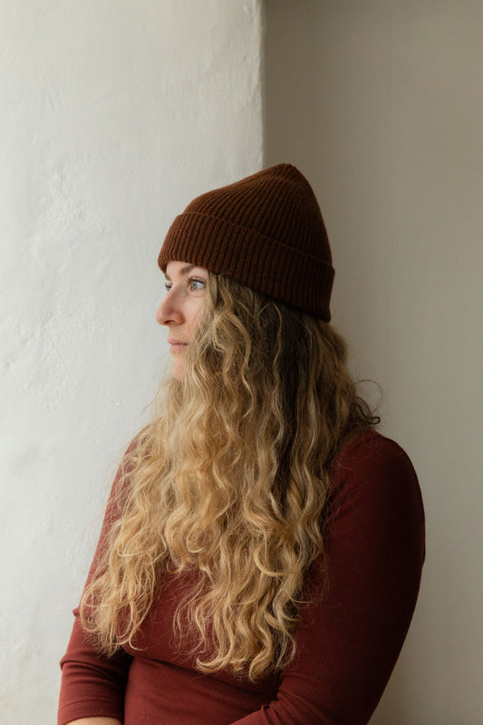 Woman in a stoat-brown ribbed merino lambswool beanie against a white wall