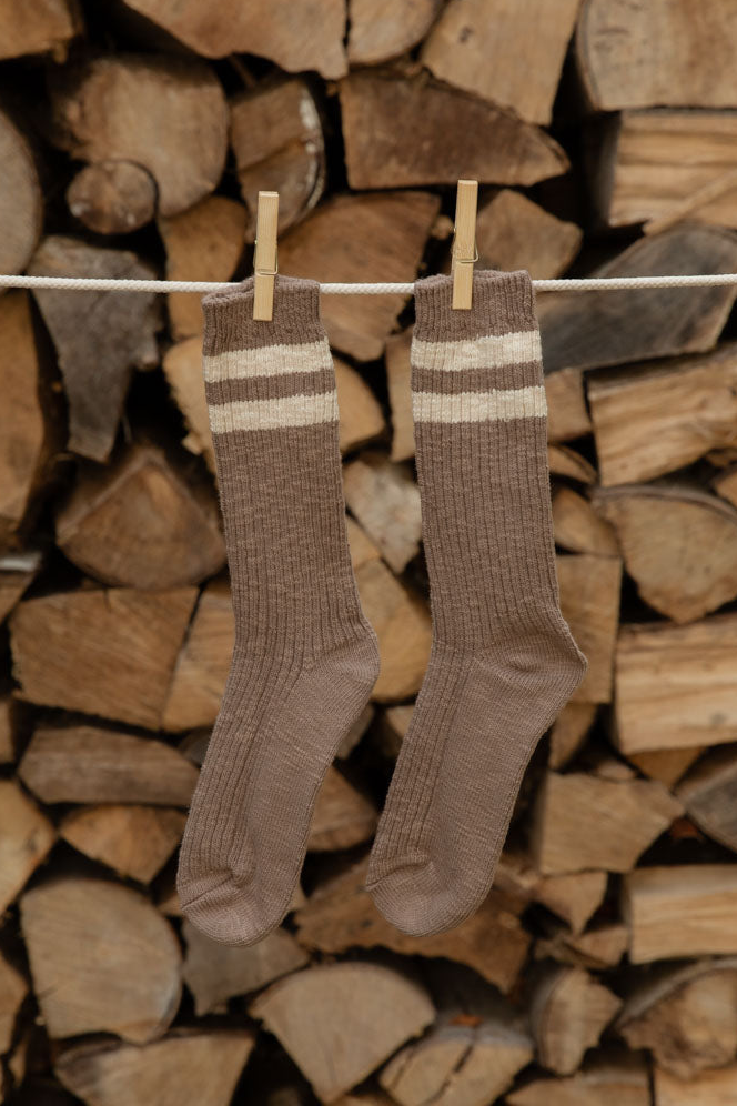 Le Bon Shoppe Cottage Socks in Varsity Stripe, brown with cream stripes, pegged on a line against logs