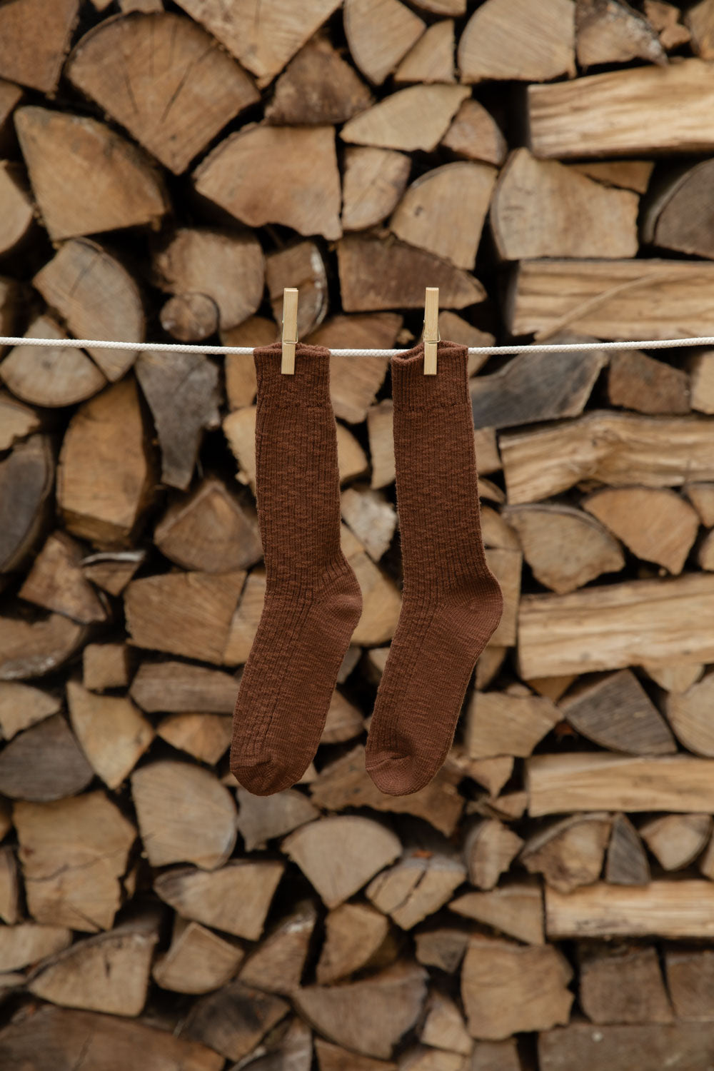 Le Bon Shoppe Cottage Socks in Bear, chocolate brown open knit, pegged against firewood