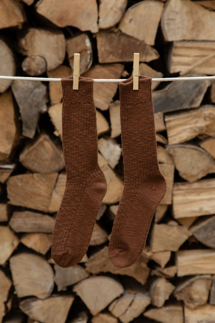 Le Bon Shoppe Cottage Socks in Bear, chocolate brown open knit, pegged against firewood