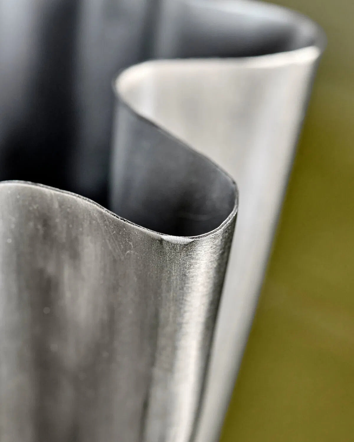 A close up image of the curves on the edge of a small, brushed silver flood vase.