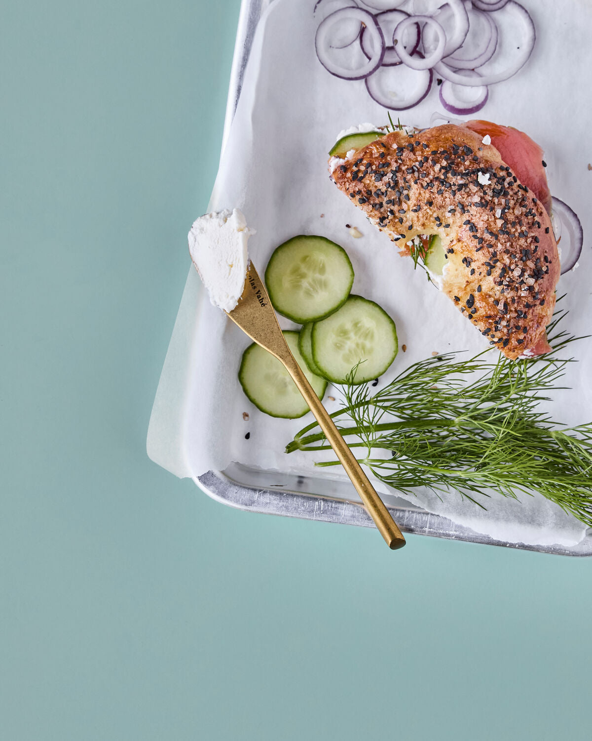 Antique gold butter knife with cream cheese beside a bagel, cucumber and dill