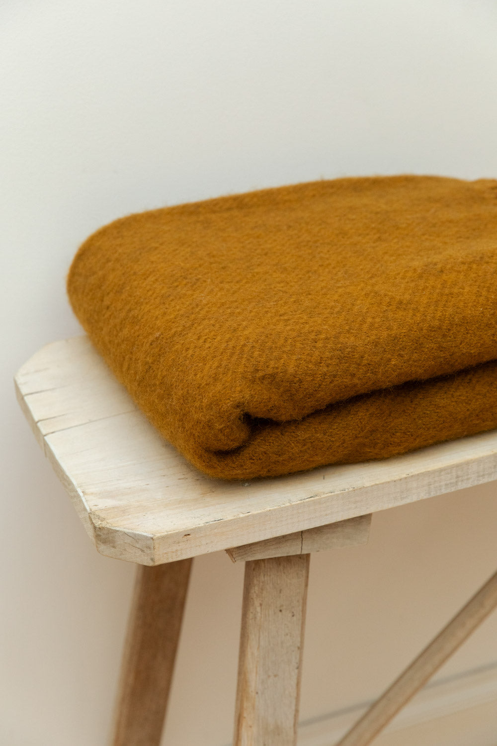 Close-up of Caramel Gotland wool blanket in mustard gold showing soft texture on a rustic pale wood table.