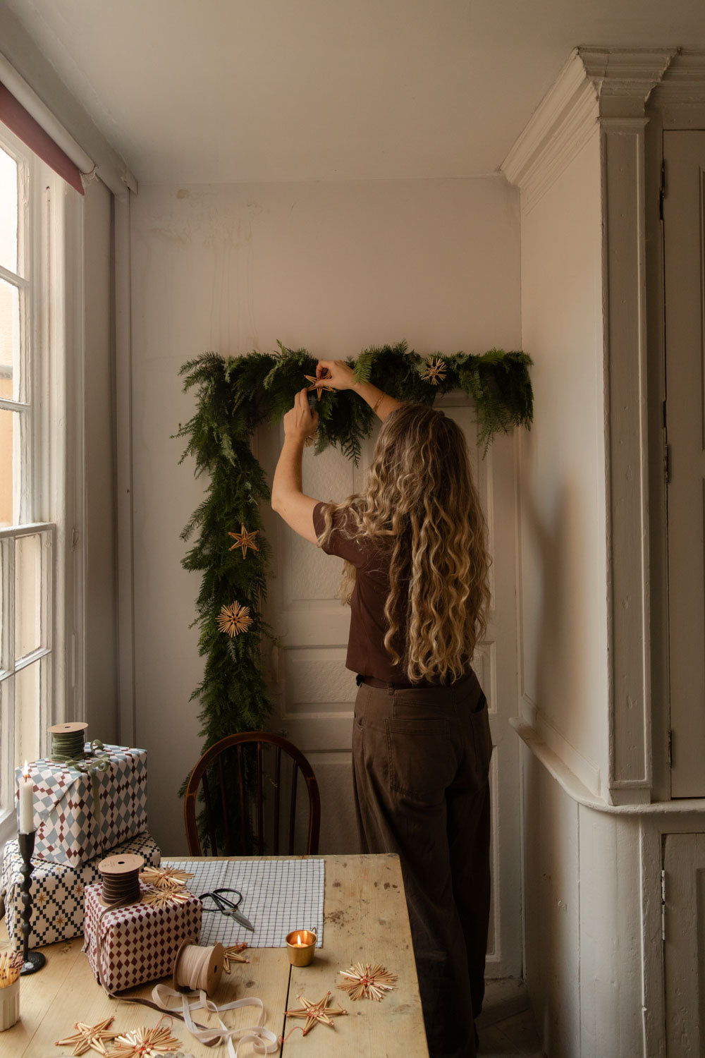 Woman adding straw stars to a fresh foliage garland around a kitchen door
