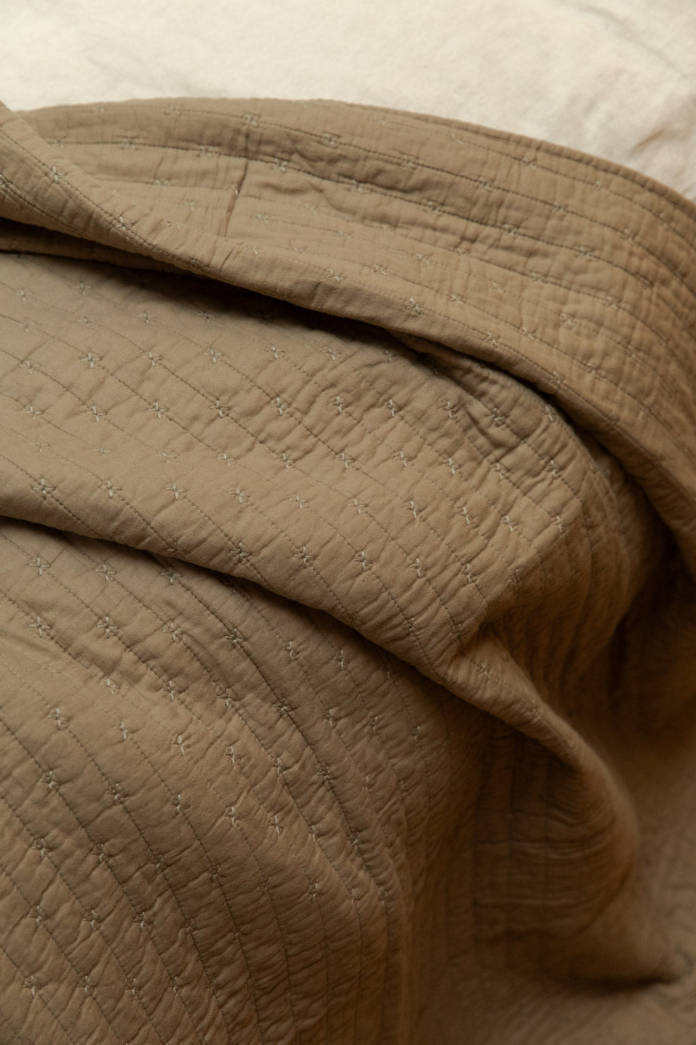 Close detail of cotton cross stitch quilt in vintage linen draped on a bed, showing fine grid stitching and soft stone-washed texture.