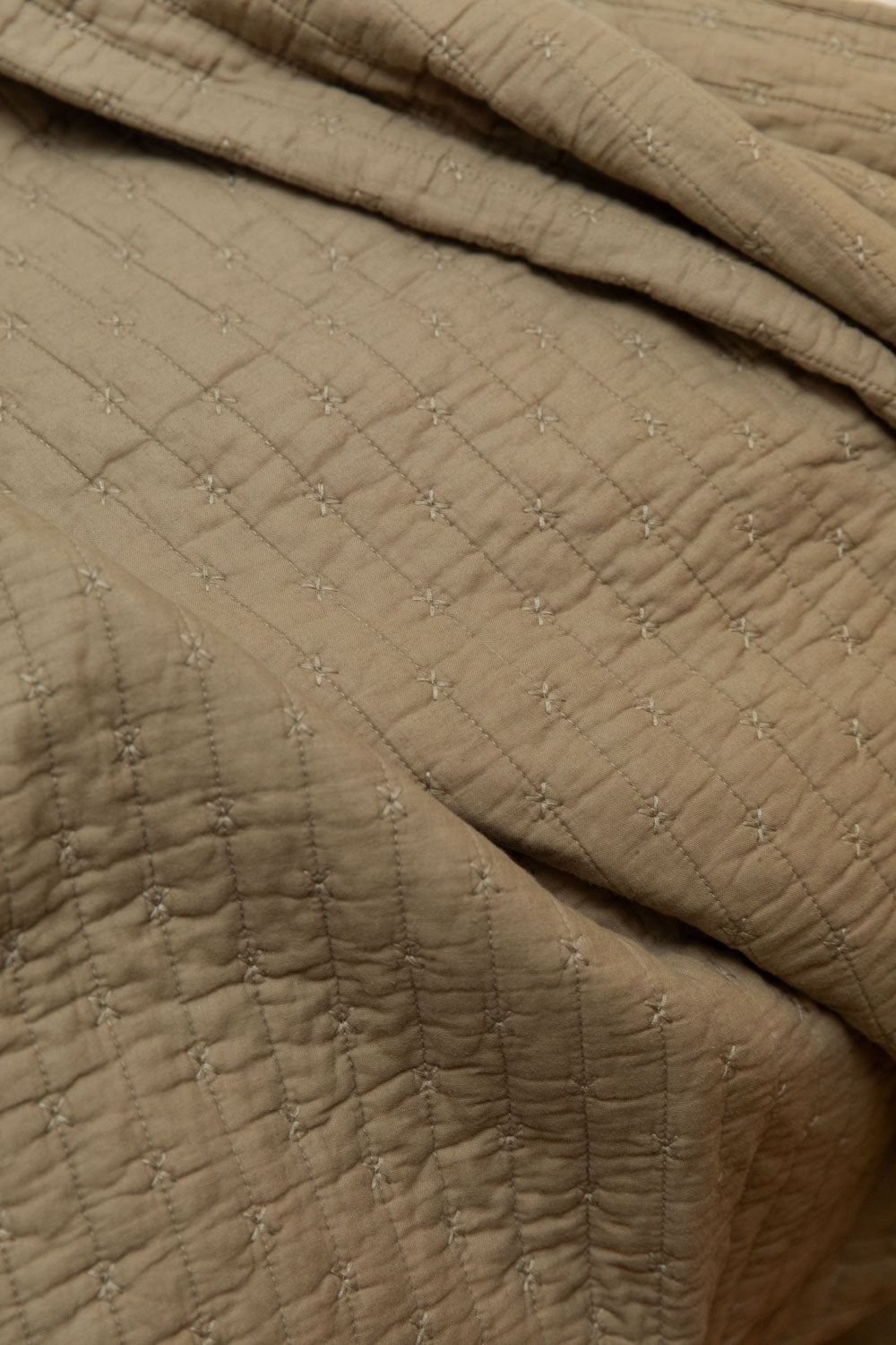 Flat lay close detail of cotton cross stitch quilt in vintage linen showing fine grid stitching and softly crinkled stone-washed surface.