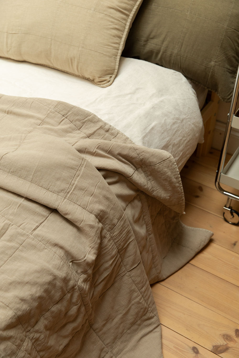 Close detail of cotton quilts in vintage linen neatly folded and stacked on a pine shelf, showing quilted stitch texture and tonal colour.