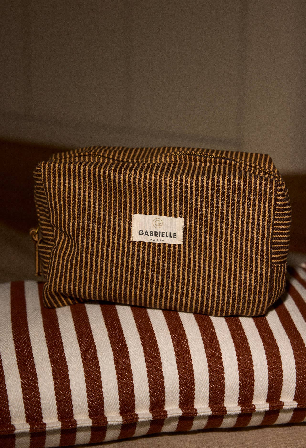 Brown striped pouch with a Gabrielle Paris label sitting on a striped fabric cushion.