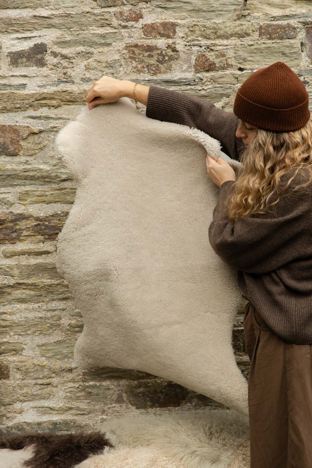 Short, dense cream British sheepskin rug in Moonlight held up against a stone wall to show its shape