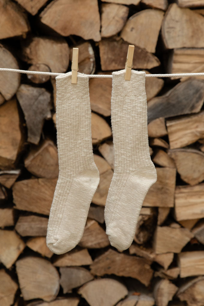 Le Bon Shoppe Cottage Socks in Oatmeal, cream open knit, hanging from wooden pegs against stacked logs