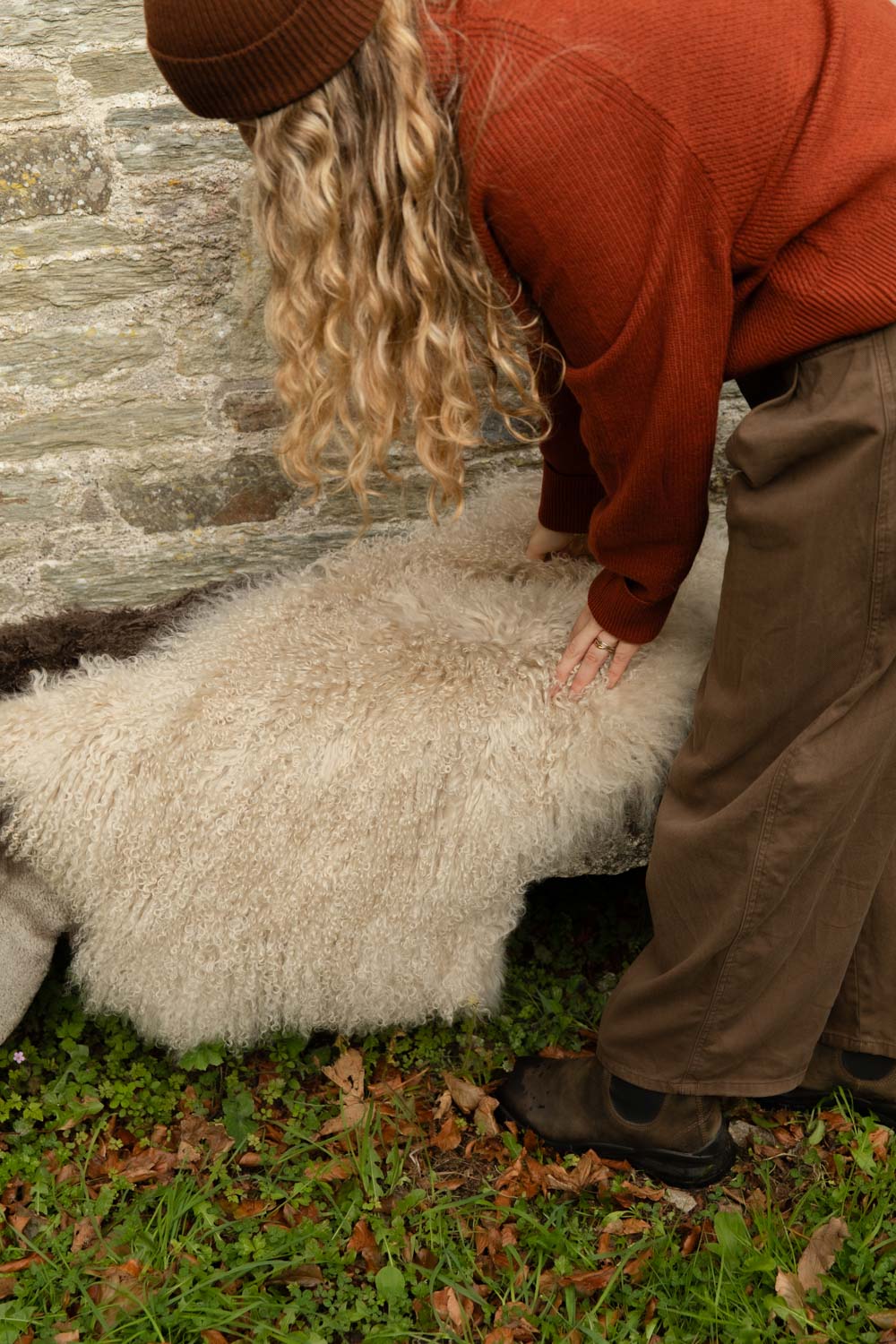 Woman smoothing a long, curly cream Tibetan sheepskin rug laid out on a stone bench outdoors