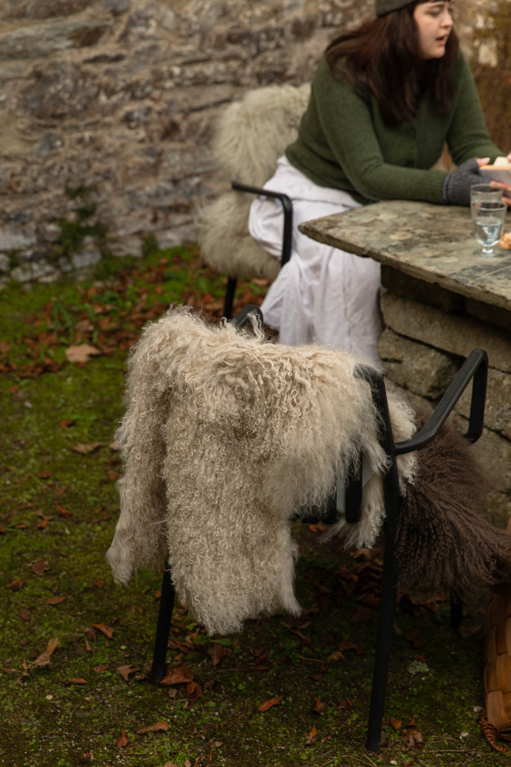 Long, curly cream Tibetan sheepskin rug draped over a black chair at an outdoor stone table in the garden