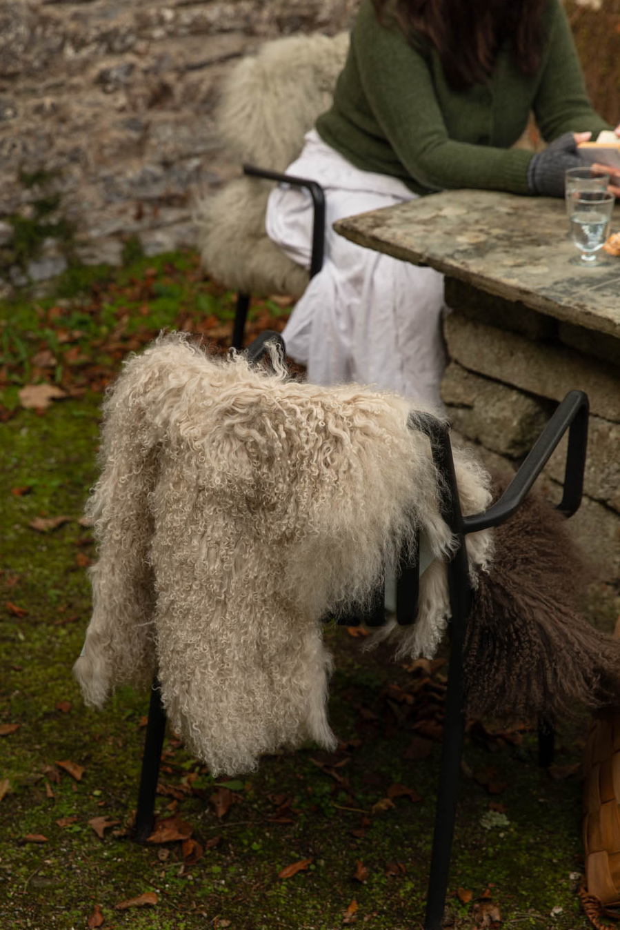 Long, curly cream Tibetan sheepskin rug draped over a black chair at an outdoor stone table in the garden