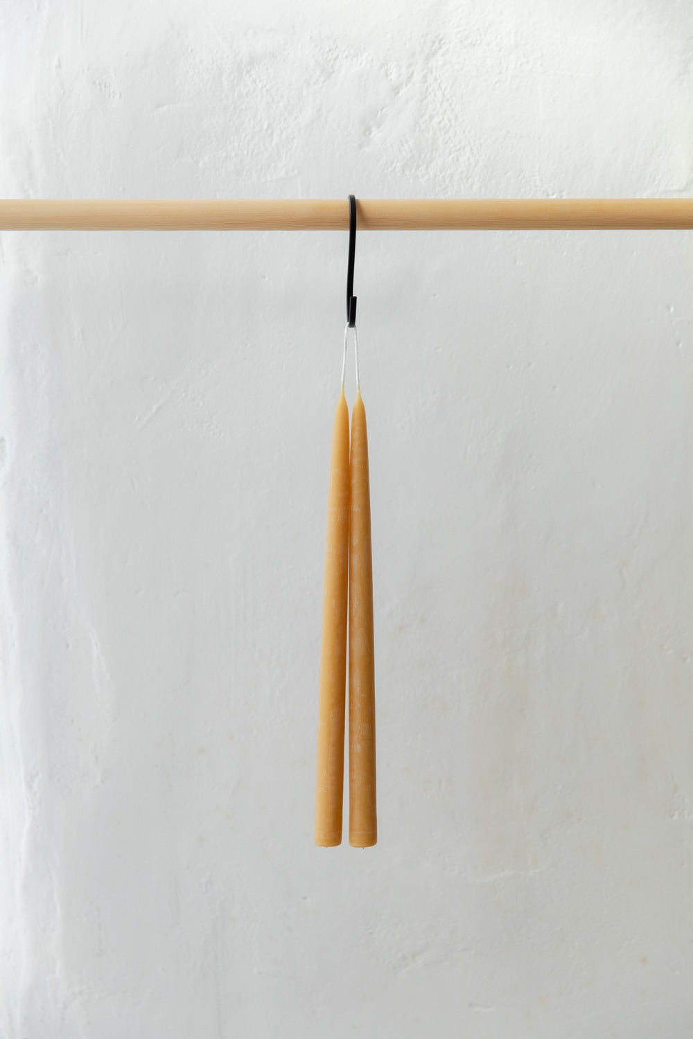 Two tall, thin, beeswax candles hanging from a wooden rod against a white background