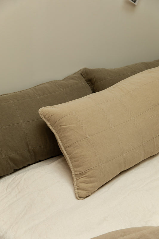 Eucalyptus green and fog quilted rectangular headboard cushions layered on a white linen bed against a soft grey-green wall