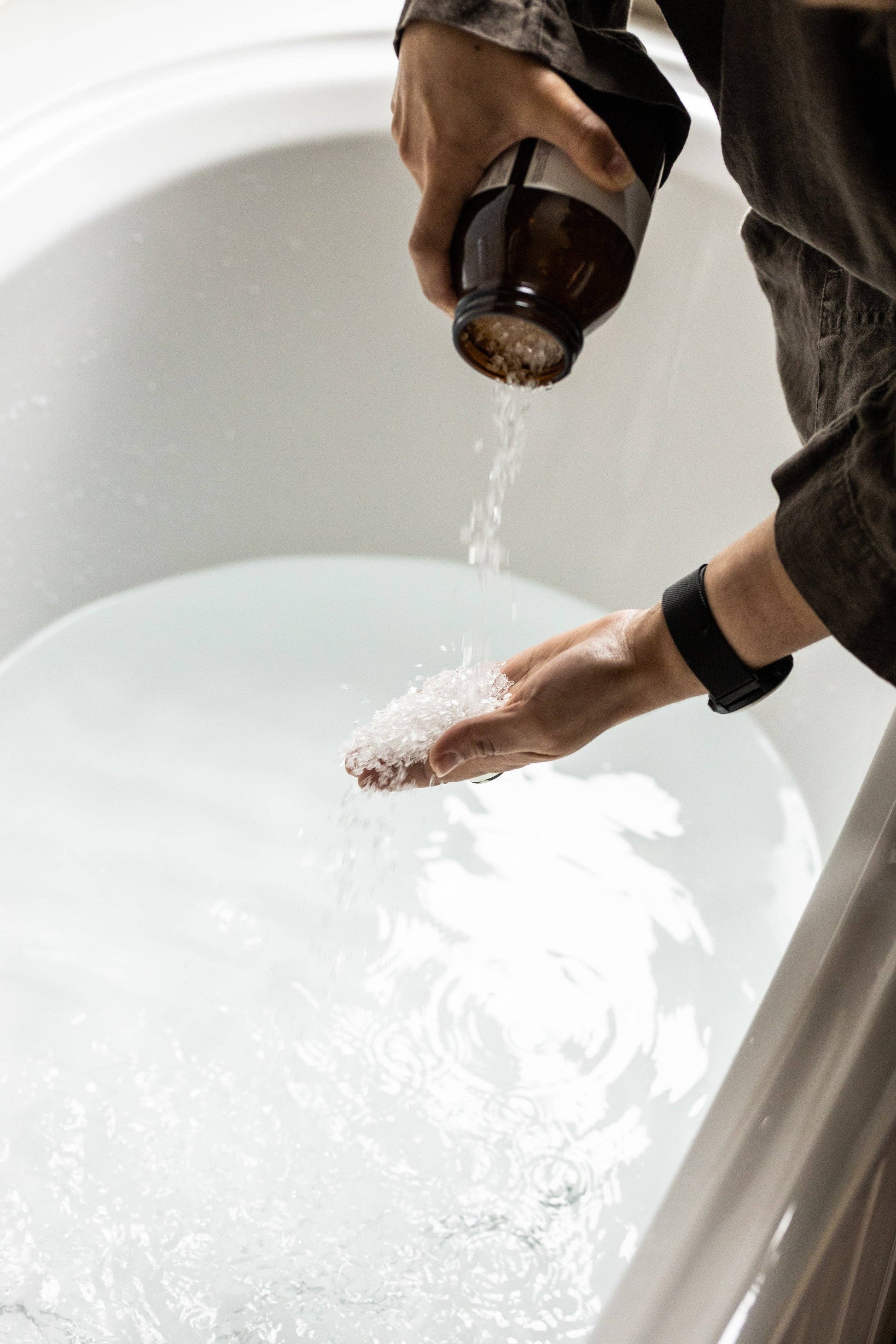Hands pouring Harvest bathing salts from amber jar into white bath