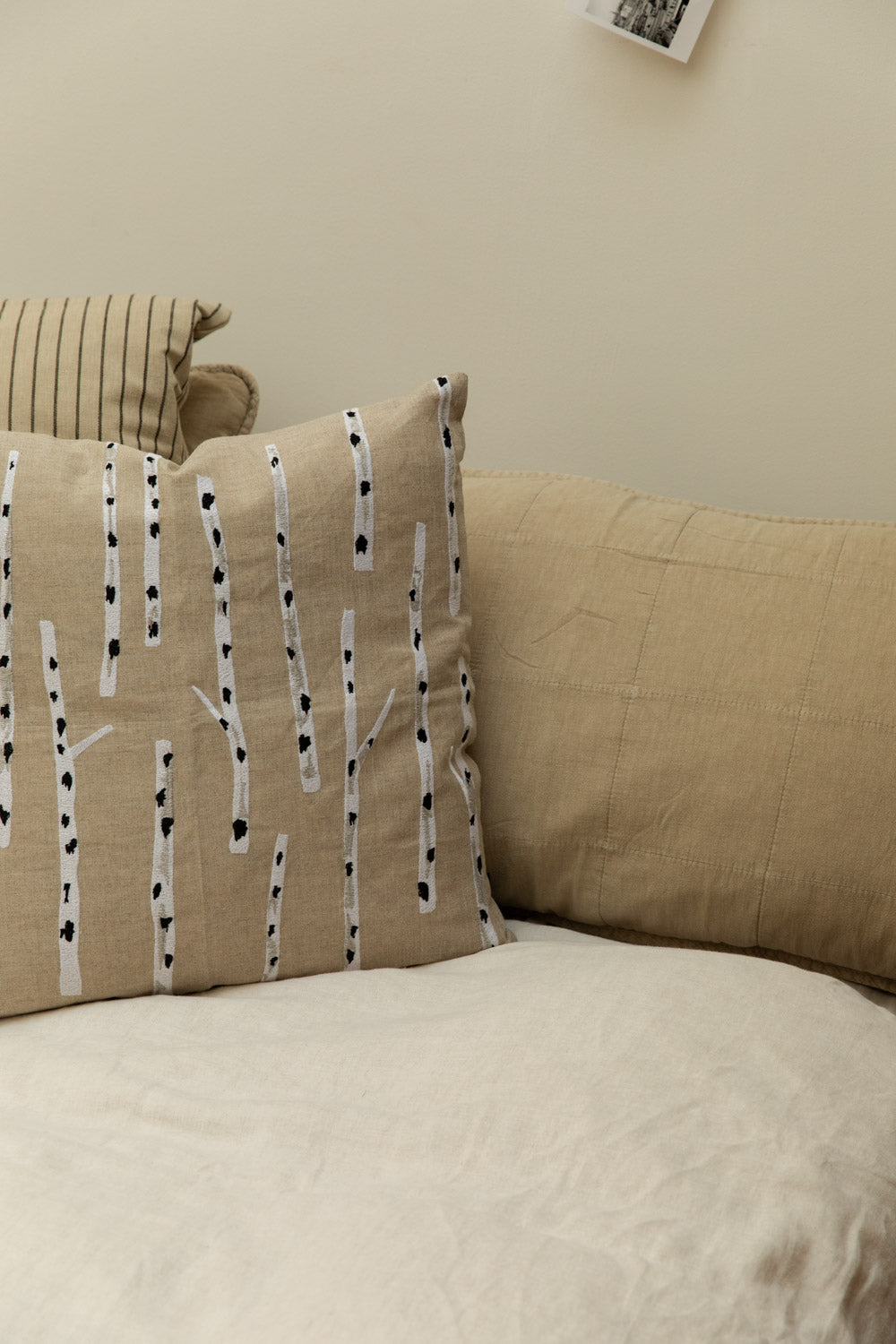 Close-up of Fine Little Day Birch embroidered linen cushion in sand and white propped against a fog linen headboard cushion with Kare stripe cushion on a white linen bed.
