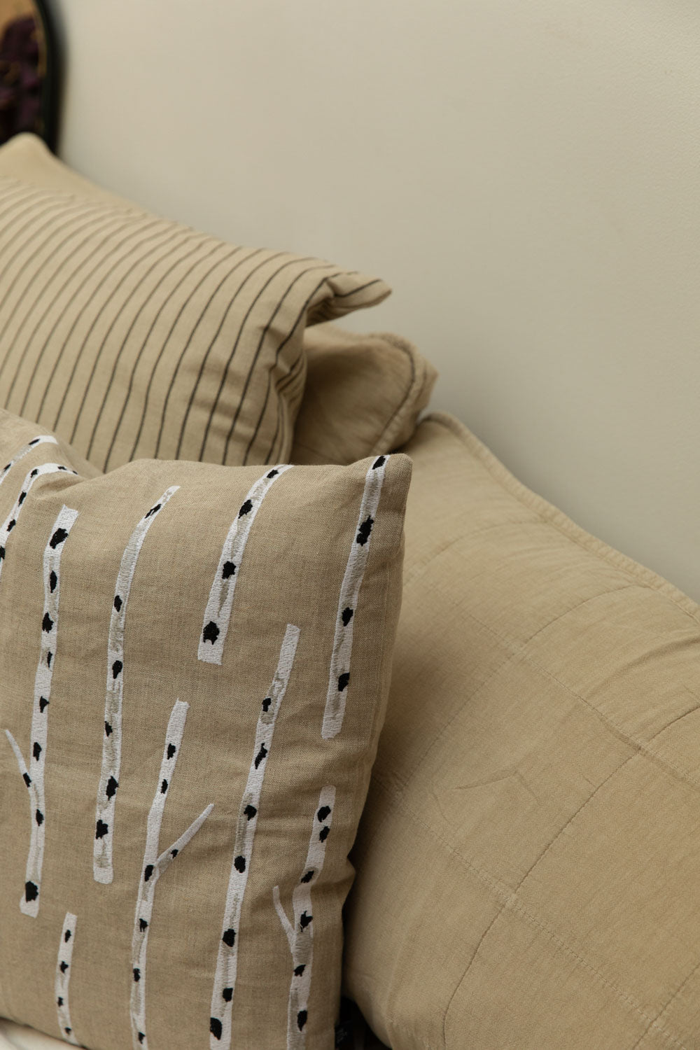 Close-up detail of Fine Little Day Birch embroidered linen cushion in sand showing white and black birch tree embroidery against fog linen headboard cushion and Kare stripe cushion.