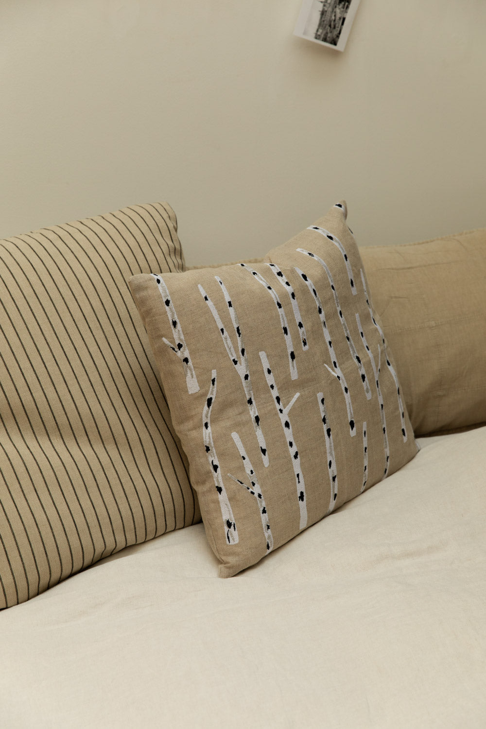 Fine Little Day Birch embroidered linen cushion in sand and white with Kare stripe cushion and fog linen headboard cushion styled on a white linen bed.
