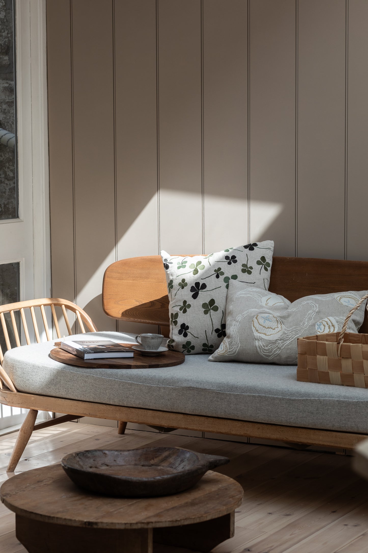 A linen coloured cushion with a green clover embroidery pattern on a wooden sofa in a living room.