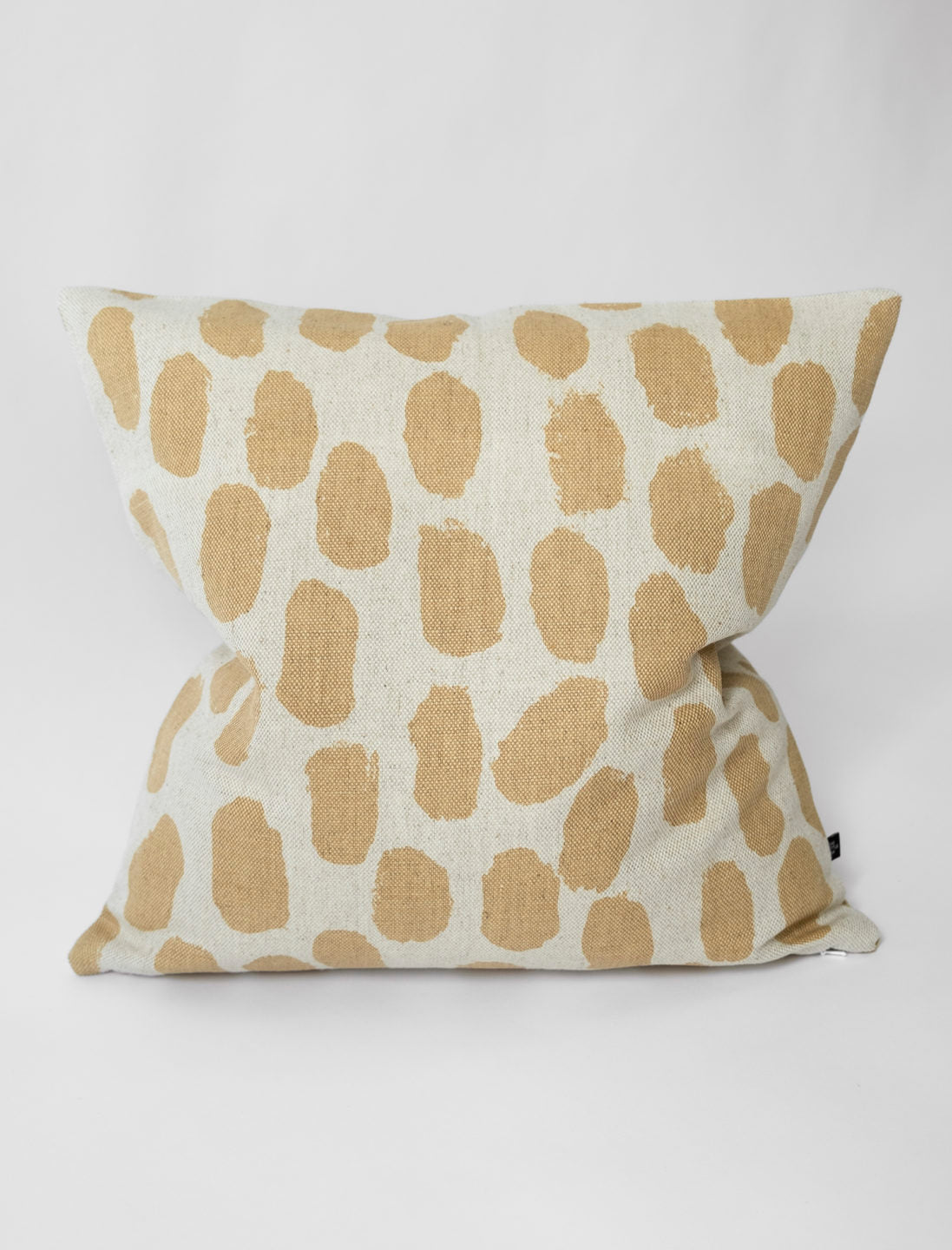 A square-shaped cushion with a beige background and a pattern of sand coloured dots.