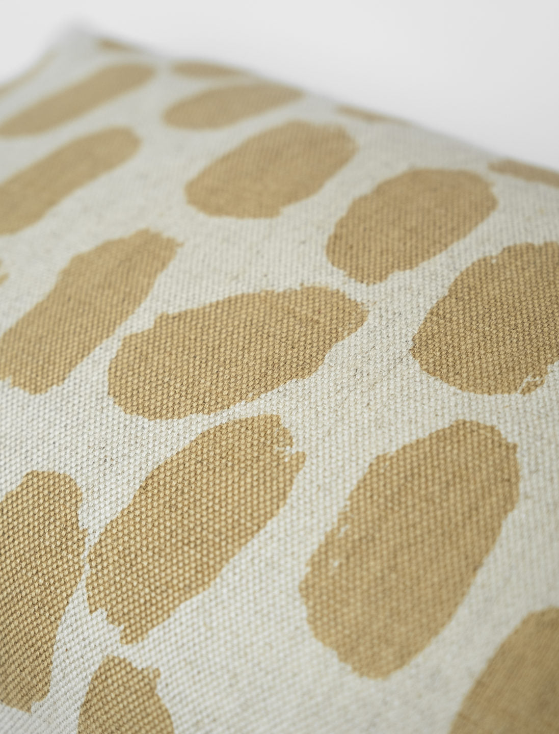 A close up of a square-shaped cushion with a beige background and a pattern of sand coloured dots.