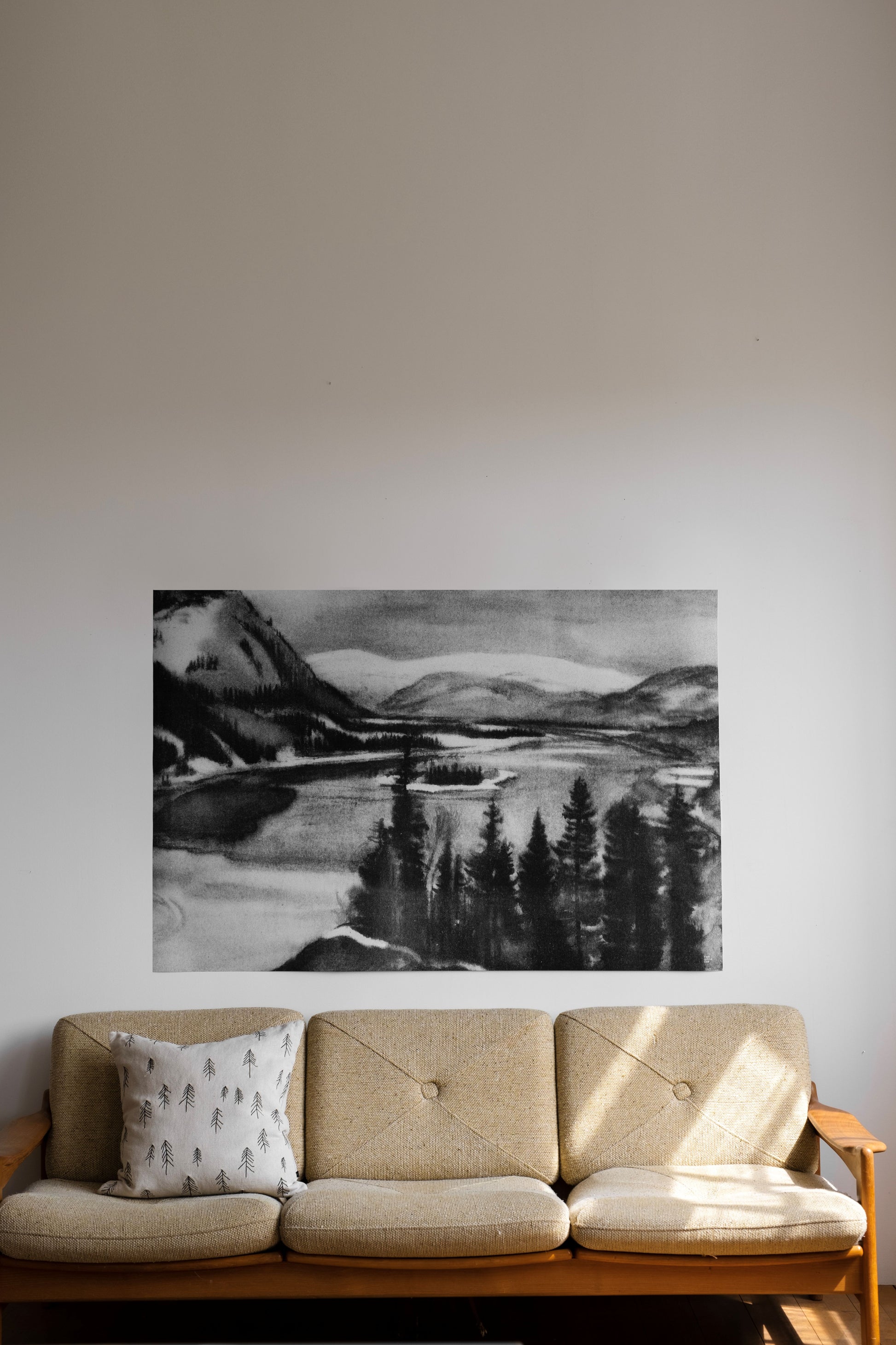 Sofa with a scenic black and white drawing of a mountain landscape on a wall.